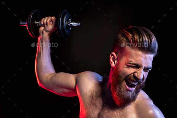 handsome bodybuilder training with dumbbell isolated on black with dramatic lighting