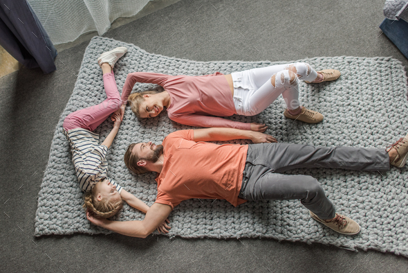 High angle view of happy family lying together on grey knitted carpet