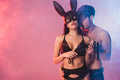 muscular man near seductive girl in mask with bunny ears holding flogging whip on pink with smoke - PhotoDune Item for Sale