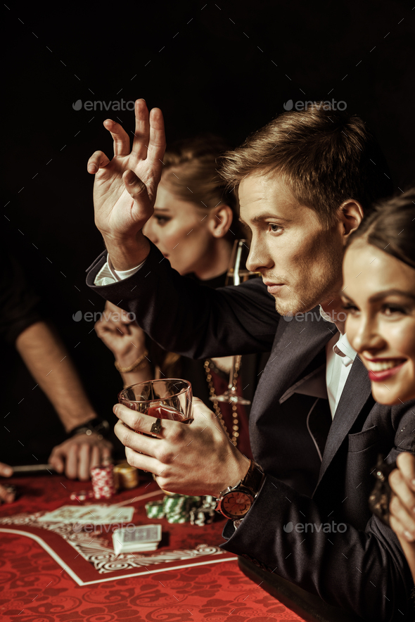 Elegant young smiling people drinking alcohol at poker table on black ...