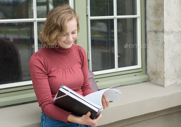 beautiful caucasian girl stands at the window of a college building and reads notes, back to school,