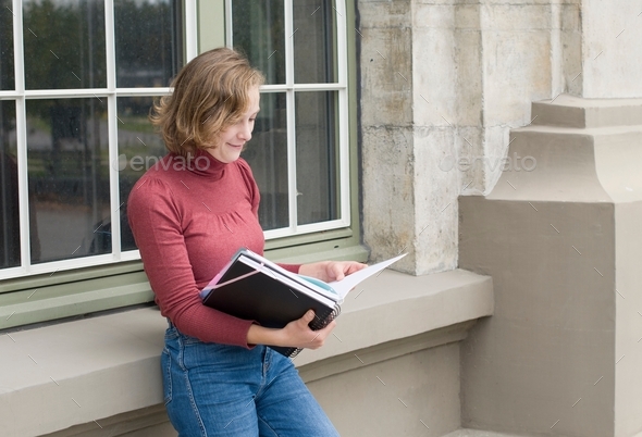 beautiful caucasian girl stands at the window of a college building and reads notes, back to school,