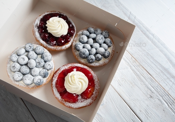 different pastries in a box, fresh cakes with berries and whipped cream, sweet dessert home delivery