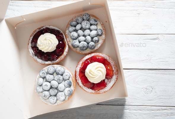 different pastries in a box, fresh cakes with berries and whipped cream, sweet dessert home delivery