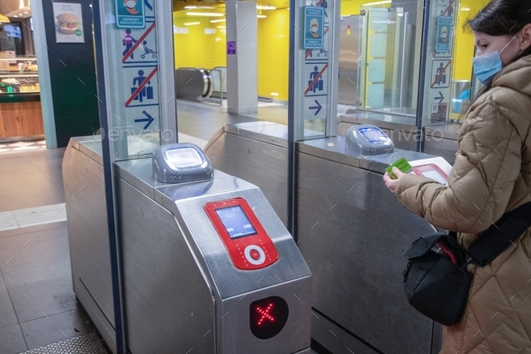a young woman in a mask goes through the loket to the metro station and pays card using a scanner