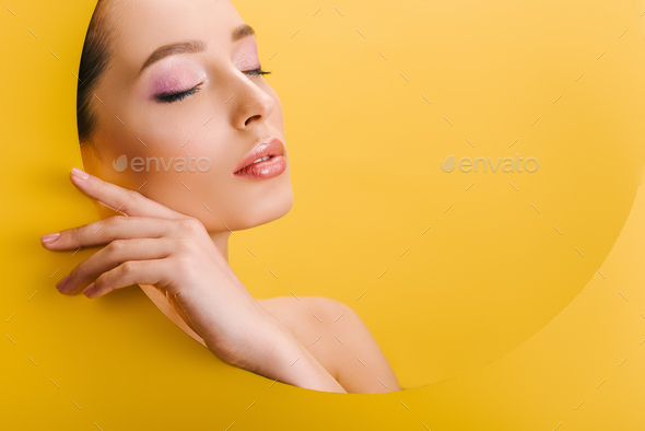 portrait of beautiful naked woman with shiny makeup in paper round hole with hand and closed eyes