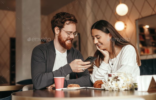 Joyful couple using smartphone while relaxing in cafe