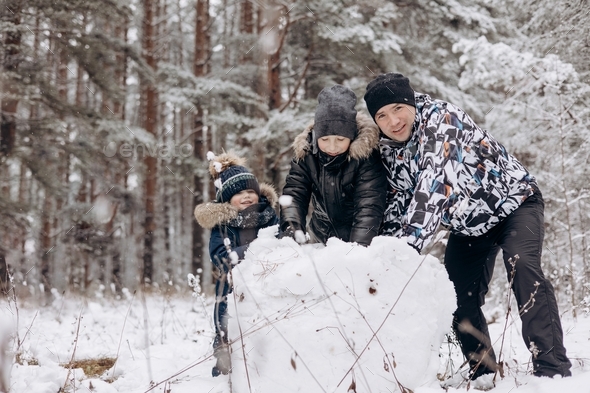 Happy father and sons making big snowball together for snowman in snowy ...