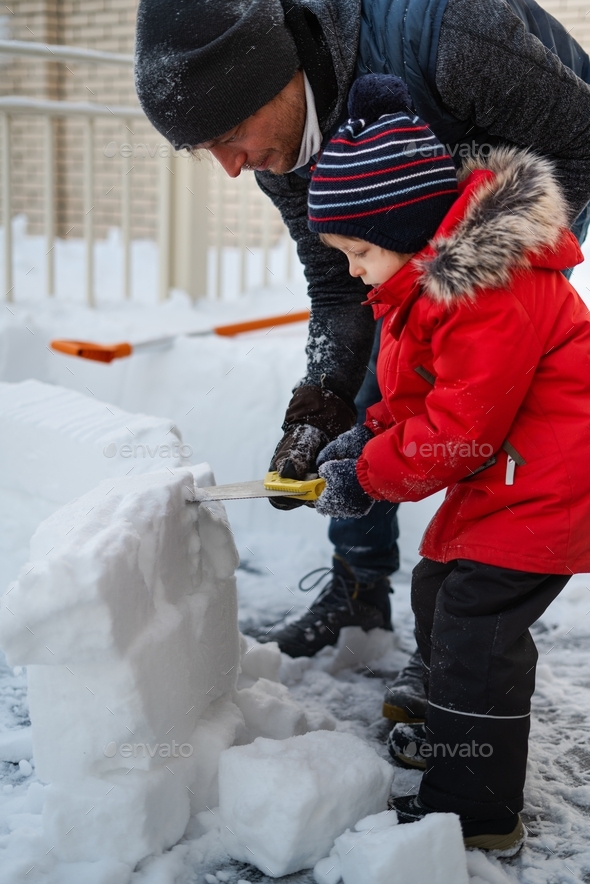 Dad and son together building an igloo out of snow bricks. Outdoor