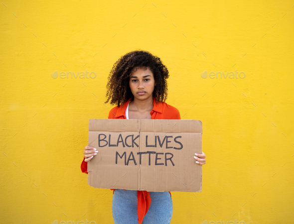 Serious young african american woman looking at camera holding a sign that says black lives matter.