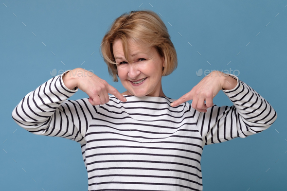 Happy mature woman pointing fingers at herself. Select me please concept.