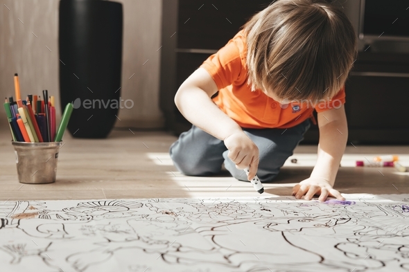  Cute little boy drawing with felt pens on floor at home. Early education concept.