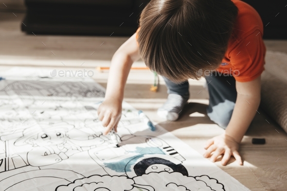 Cute little boy drawing with felt pens on floor at home. Early education concept.