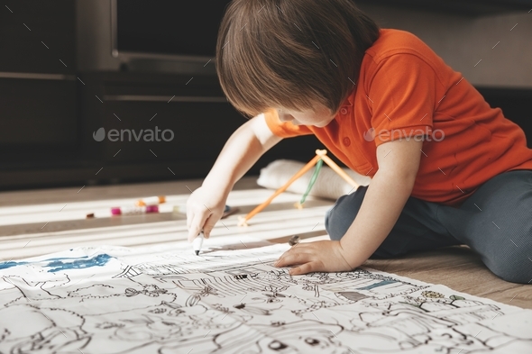 Cute little boy drawing with felt pens on floor at home. Early education concept.