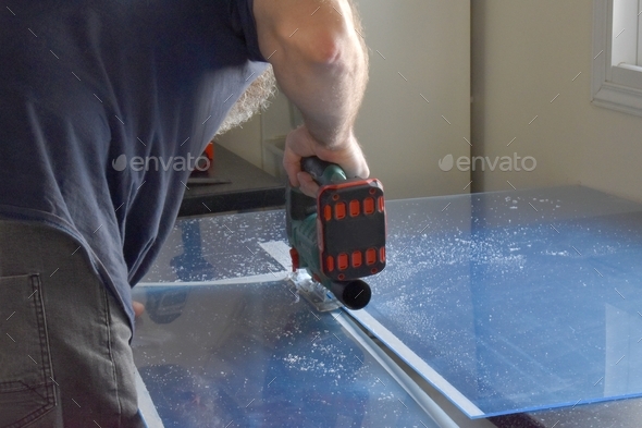 Man using a cordless jigsaw tool to cut acrylic sheet.