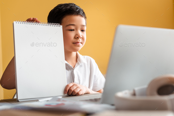 asian boy studying online with notepad and laptop at home during quarantine