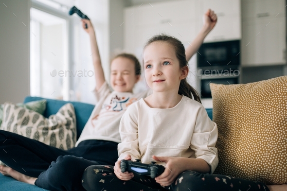 two girls are sitting on a sofa and playing a play station, sisters are playing