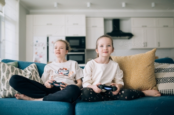 two girls are sitting on a sofa and playing a play station, sisters are playing