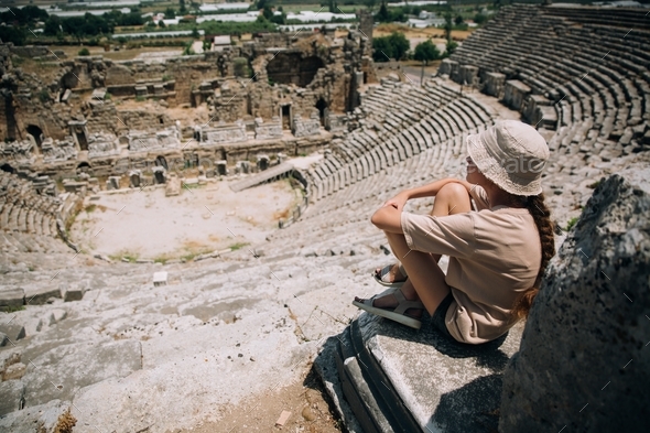 A teenage girl in a hat sits on top of an amphitheater in Perge, Turkey ...