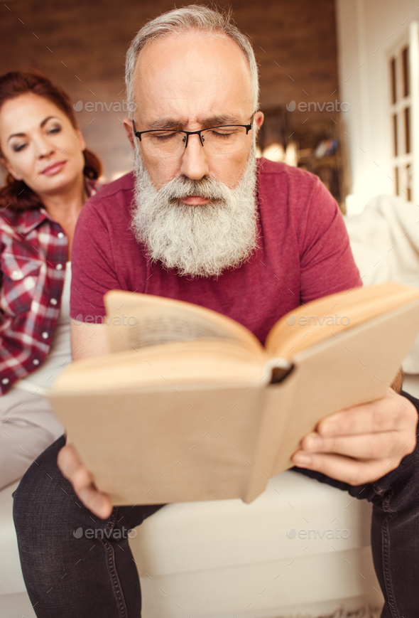 Concentrated Bearded Man Reading Book While Woman Sitting Beside Him