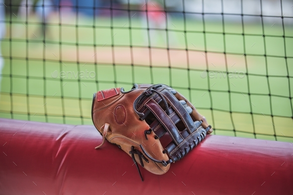 A single baseball glove sitting on top of a padded bar in a baseball dugout