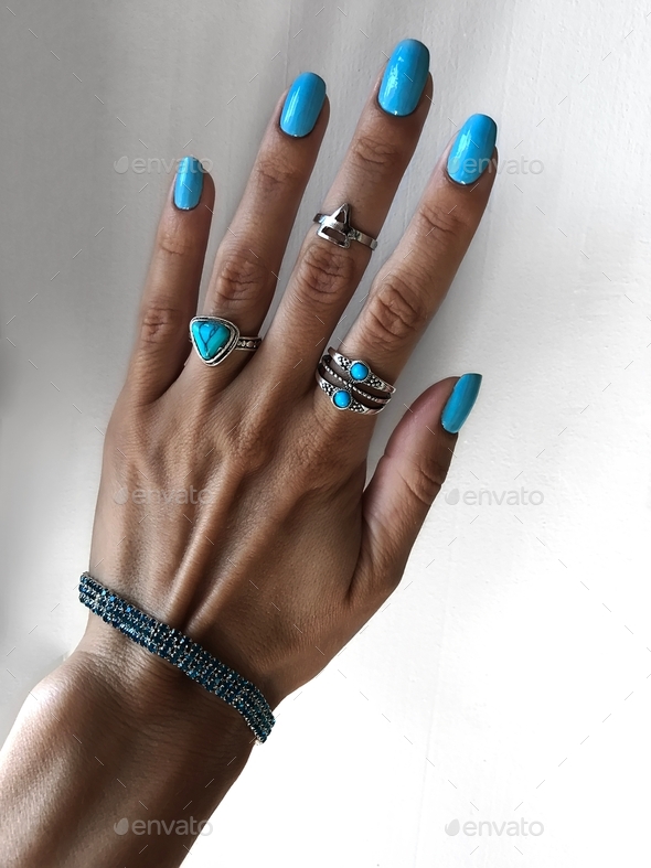 Blue nail polish and blue jewelry accessories on female hand in front of white background
