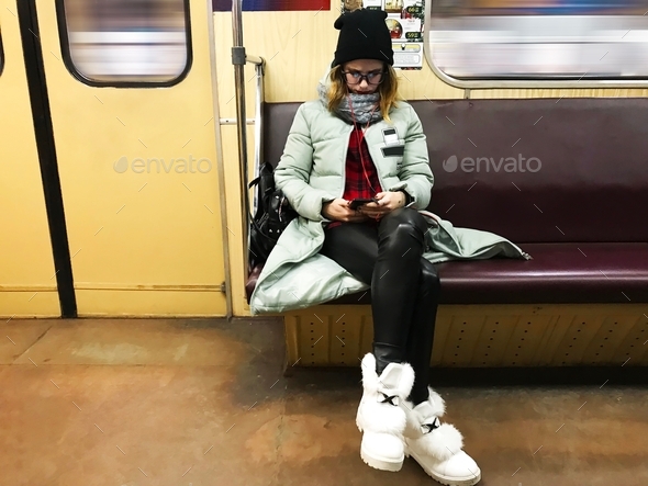 Young woman in winter clothes using mobile phone in subway train