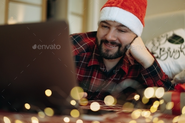 caucasian bearded handsome man in red plaid flannel shirt in santa hat chatting online