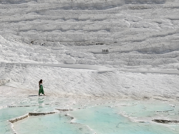 Tiny figure of a young woman walking by the white chalk landscape with blue water on the ground