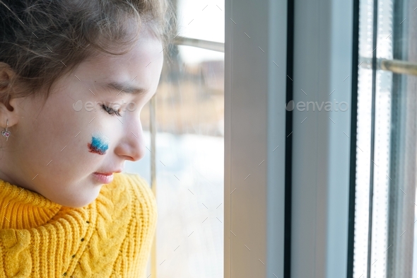 A sad child at the window with the flag of Russia, worries with tears in his eyes.