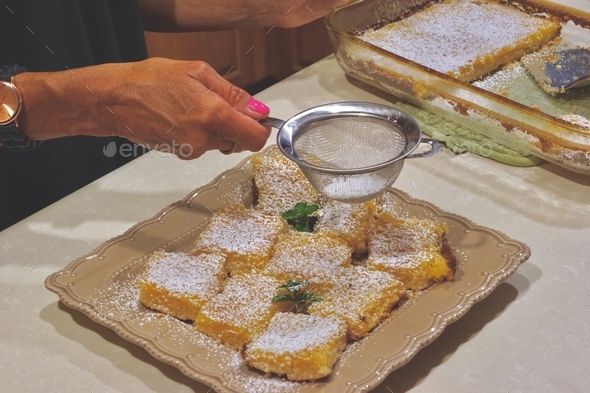 Woman putting the finishing touches on the delicious, homemade lemon squares, in the kitchen!