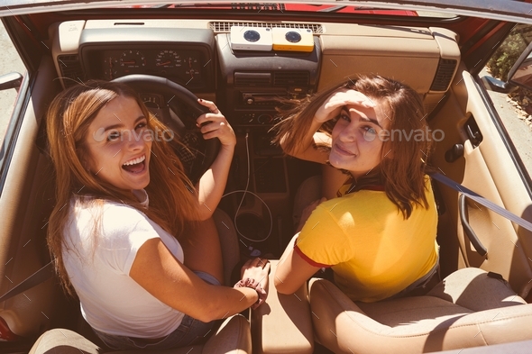 Overhead shot of two girls on a road trip in a convertible car