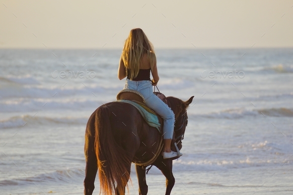 A beautiful, thoughtful photo of a woman on a horse, horseback riding on the beach by the ocean