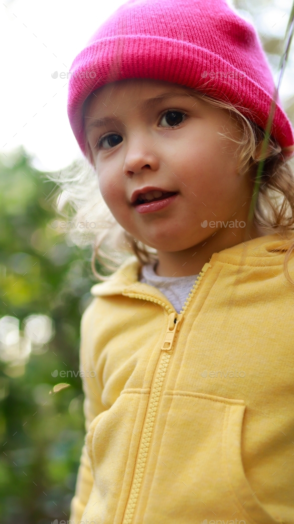 Little girl wearing yellow jacket and pink hat outdoor Stock Photo by