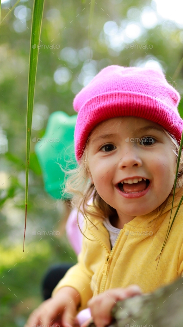 Happy little girl wearing yellow jacket and pink hat sitting on the