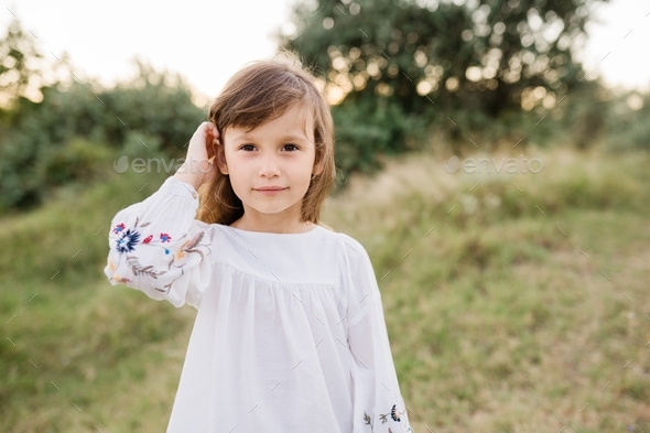 Portrait of beautiful six year old girl standing in field sunset in nature - Stock Photo - Images