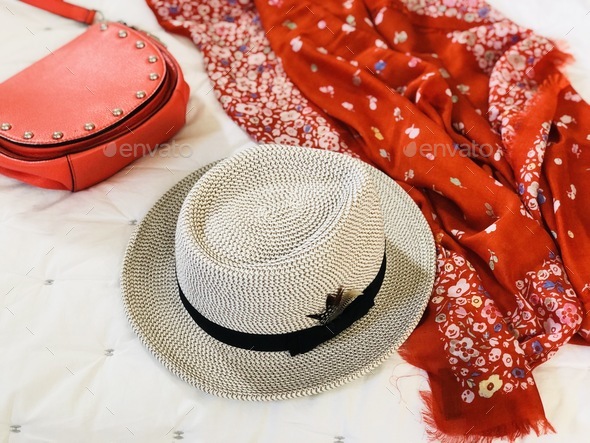 Fashion accessories woman’s fedora brimmed hat bright orange scarf and purse handbag on a white bed