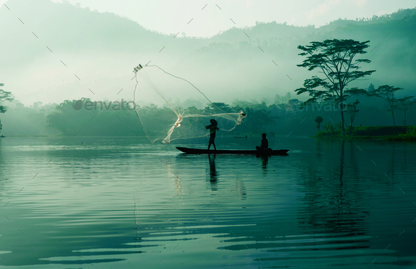 Fisherman casting out his fishing net in the river by throwing it high up into the air early in the