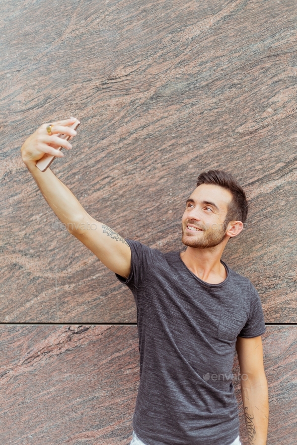 Portrait of young man standing outdoors while taking selfie - Stock Photo - Images