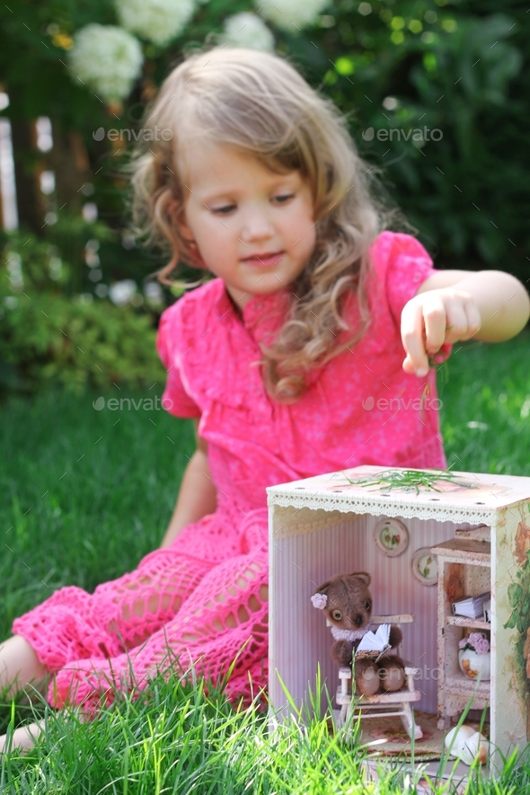 Beautiful little girl with pink dress sitting near dolls house with handmade mini teddy bear