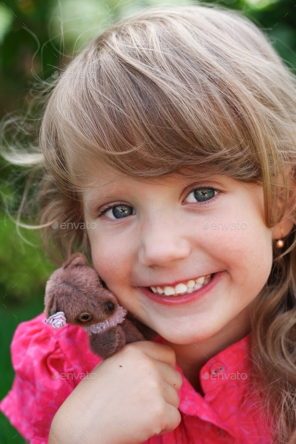 Cute smiling little girl with long blond hair in pink dress hugging mini handmade teddy bear