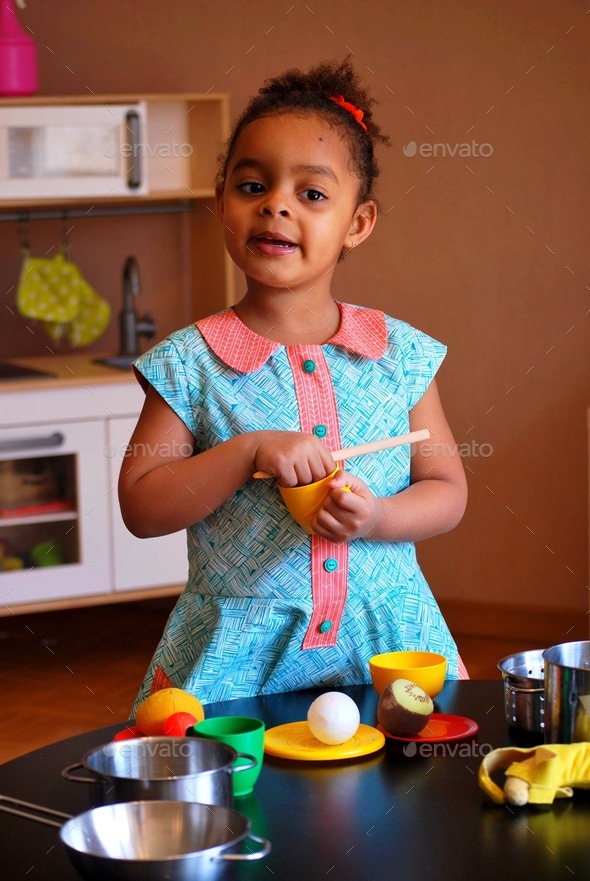 Girl of mixed race / black playing in toy kitchen Stock Photo by