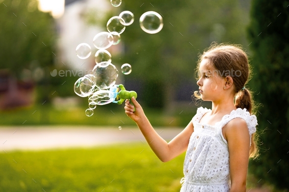 Little girl using bubble machine to create soap bubbles. Summer fun concept