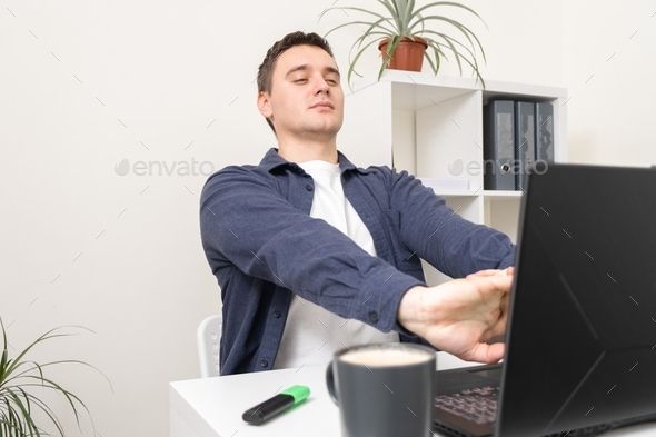 A man kneads his neck while sitting at the workplace.
