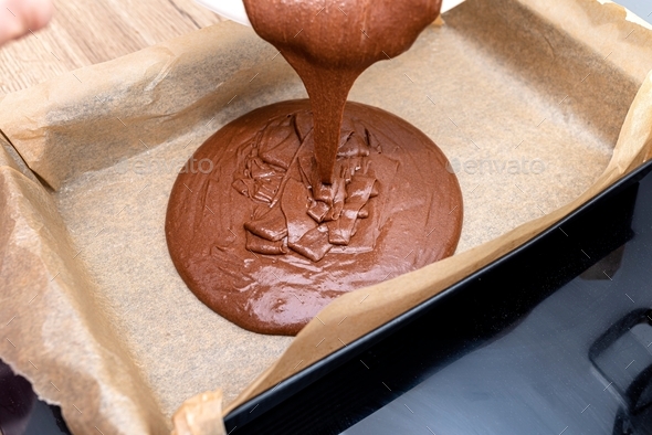 Pouring a liquid thick mass of cocoa dough onto a baking sheet lined with baking paper.