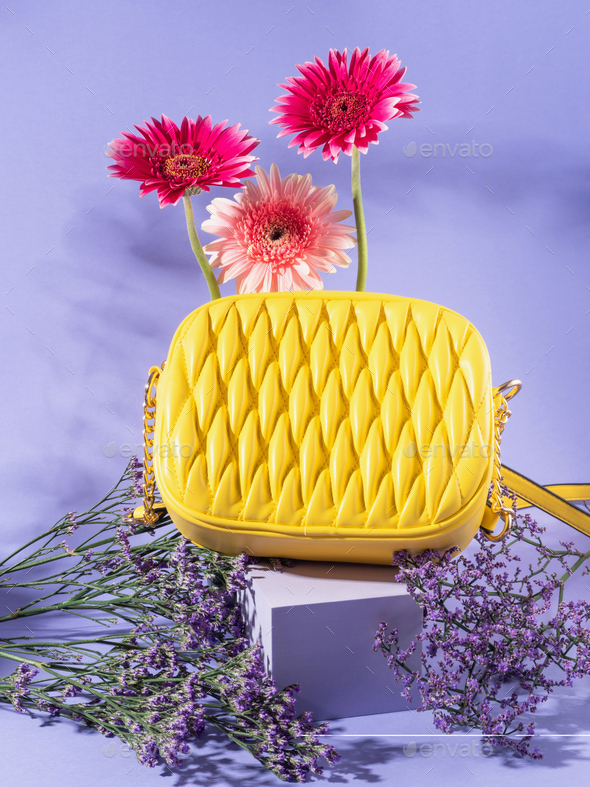 Yellow fashion lady handbag with pink flowers on purple podium