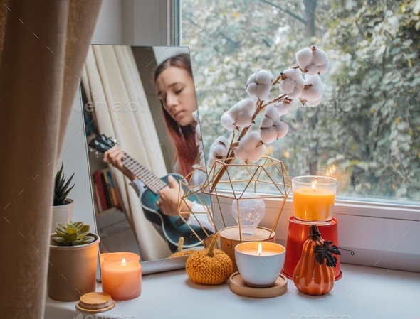 Girl sits in her room on a window sill decorated for the holiday and plays the ukulele.