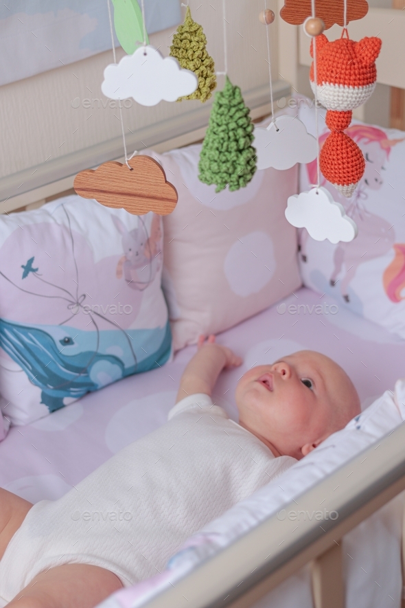 Newborn baby girl lies in a crib and looks up at hanging toys Stock ...