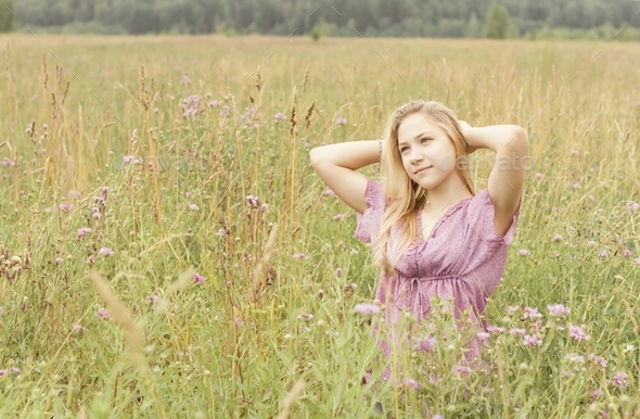 a Caucasian blonde girl in a purple blouse walks through a field with purple cornflowers