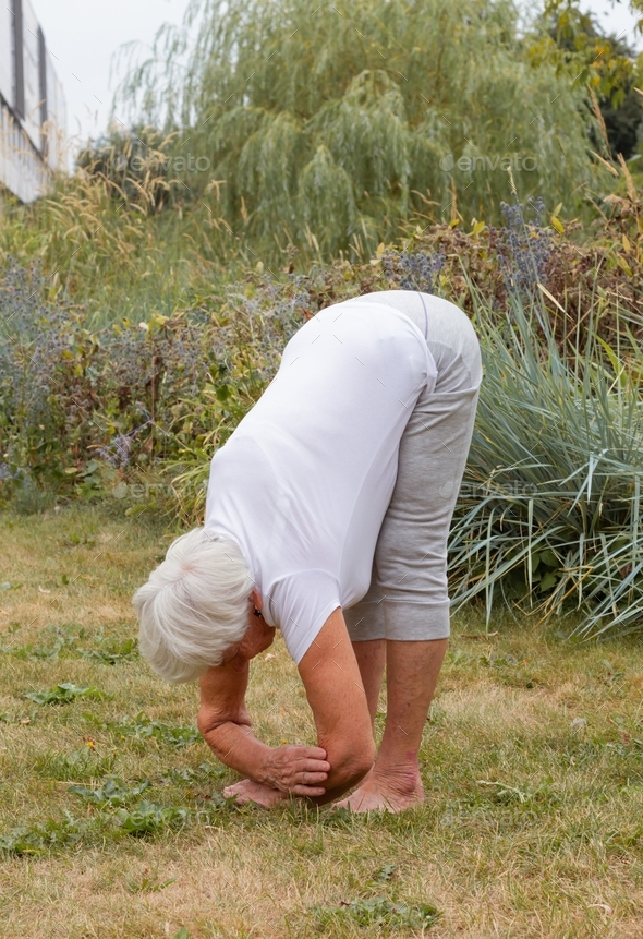 A positive elderly, athletic woman does an exercise front bend, front